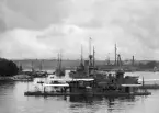Militärmarin uppslutning i Stockholm, sannolikt i samband med Stockholmsutställningen 1897. Vid Skeppsholmen ses HM pansarbåt John Ericsson samla några systerfartyg. I fonden Strandvägens pampiga husrad.
