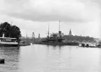 En av marinens pansarbåtar vid redden intill Skeppsholmen i Stockholm. Bortom fartyget skymtar Nordiska museet. I bildens högerkant skymtar en paviljong som daterar bilden till sommaren 1897 och i sammanhang med Stockholmsutställningen med mässområde på Djurgården.