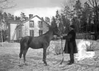 Man och häst utanför bostadshus.