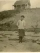 Porträtt av en kvinna, vid namn Lizzie, som står på en strand med en stuga i bakgrunden vid Wellfleet Cape cod, USA  (enligt en del av texten på baksida kort).