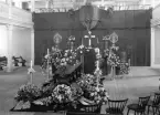 Interiör från en kyrkobegravning. Kista med blomdekorationer.