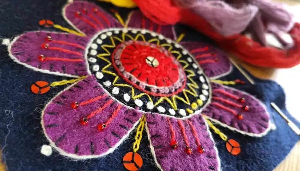 Broderad blomma i lila samt andra färger.
