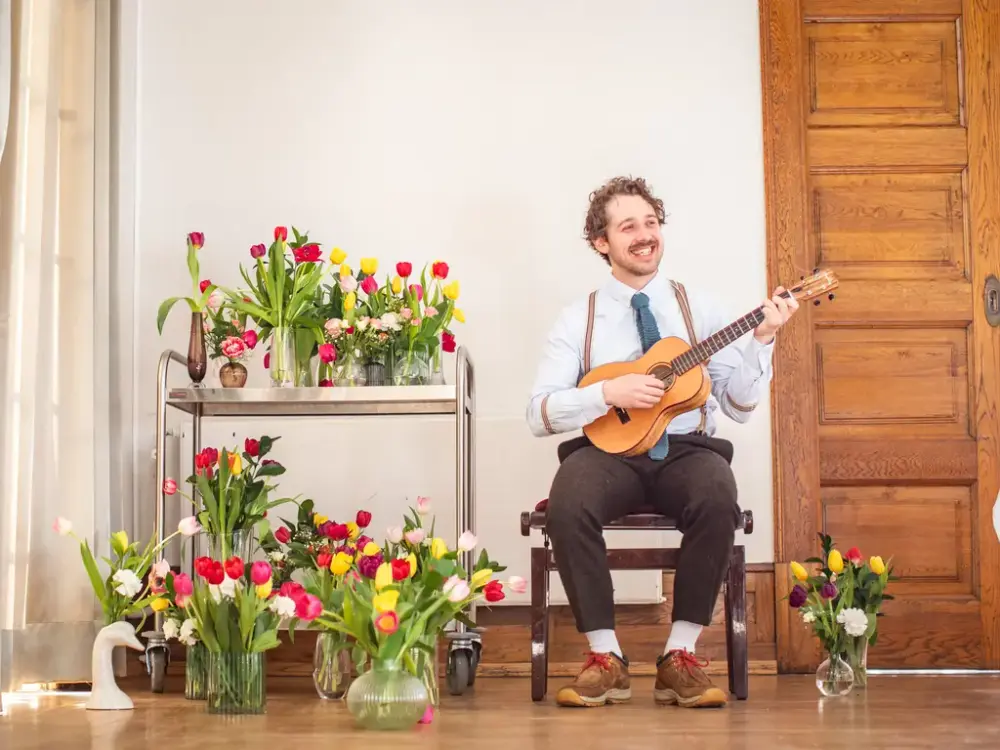 Portrett av Benjamin Kippersund sittende på en stol med ukulele i fanget