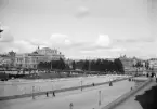 Välbekant Stockholmsvy där en månghövdad skara denna dag styrde sina steg förbi Kungliga slottet mot okänt mål. Scenen förevigades omkring förra sekelskiftet, där somligt specifikt talar för sommaren 1905.