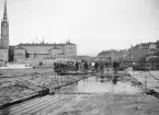 Liv och rörelse på och kring flottbron intill inloppet till Riddarholmskanalen. I fonden Riddarholmens omisskänliga siluett. Foto omkring år 1900.