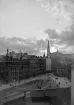 Sankt Johannes spira täcker den nedåtgående solen och gjorde ett fotografiskt panorama över Engelbrektsplan möjlig. I dunkelt sken styr några av Stockholms invånare sina steg mot enskilda mål. Foto omkring år 1900.
