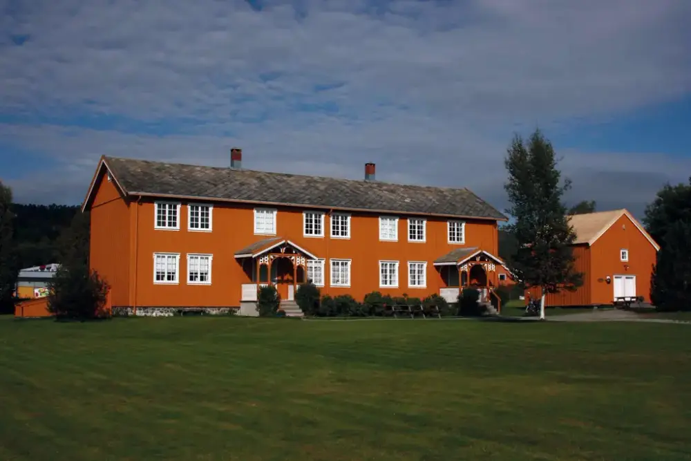 Stort okergult trebygg - trønderlån - med gressplen foran. Foto.