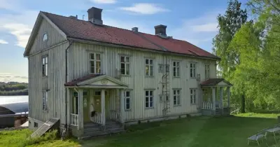 Ett äldre ljust hus med några mindre träd vid höger sida.