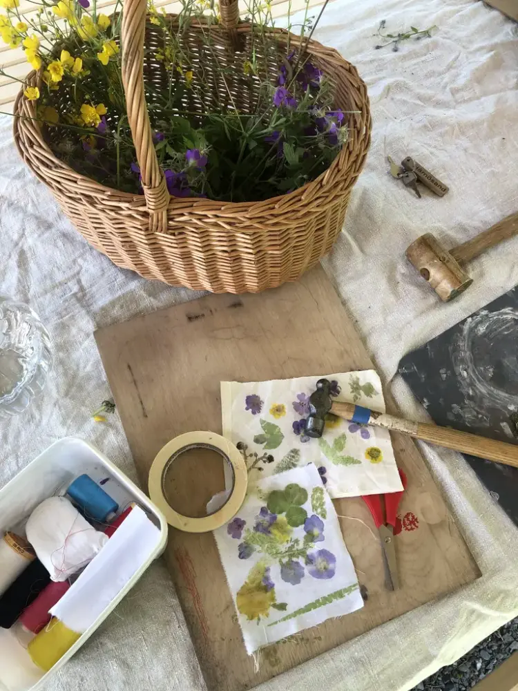 En korg med blommor, hammare, pappersark med målade blommor, en sax, en skärbräda i trä och en låda med diverse saker.