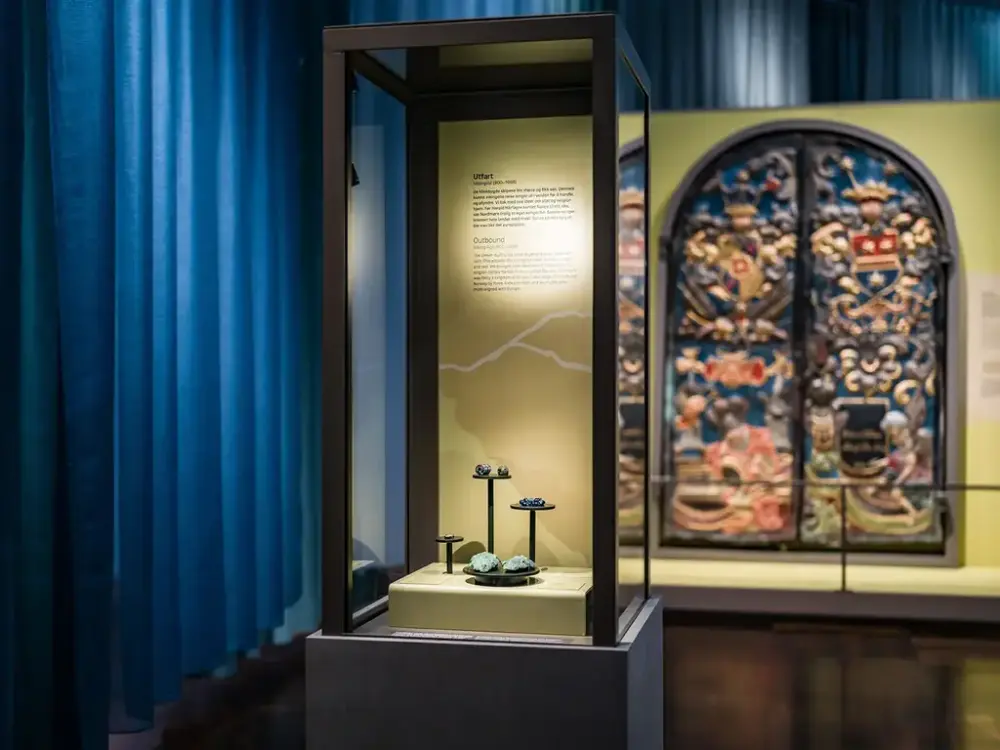 Bilde av museumsgjenstander i montre. Mørkeblå forheng i bakkant av montrene.