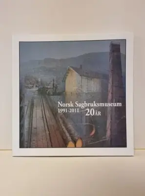 Bokomslag med fargeillustrasjon av tømmer, sagbrukspipe og et hvitt bygg i bakgrunnen. Boktittel: Norsk Sagbruksmuseum 1991-2011 - 20 år. Foto.