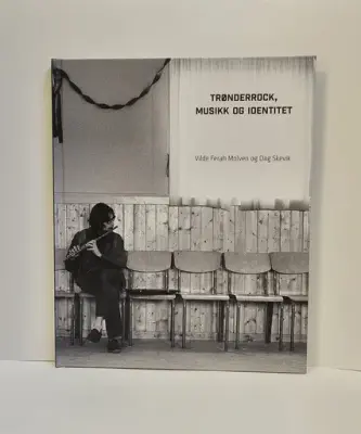 Bokomslag med et svart-hvitt bilde av en musiker som spiller fløyte mens han sitter på en enkel stol. Boktittel: Trønderrock, musikk og identitet. Foto.