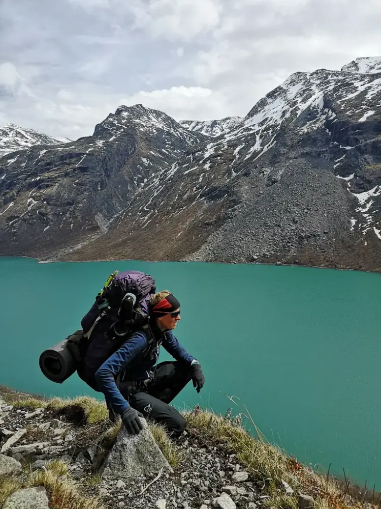 Gina johansen på en bergskrent foran et bresjø med fjell i bakgrunnen 