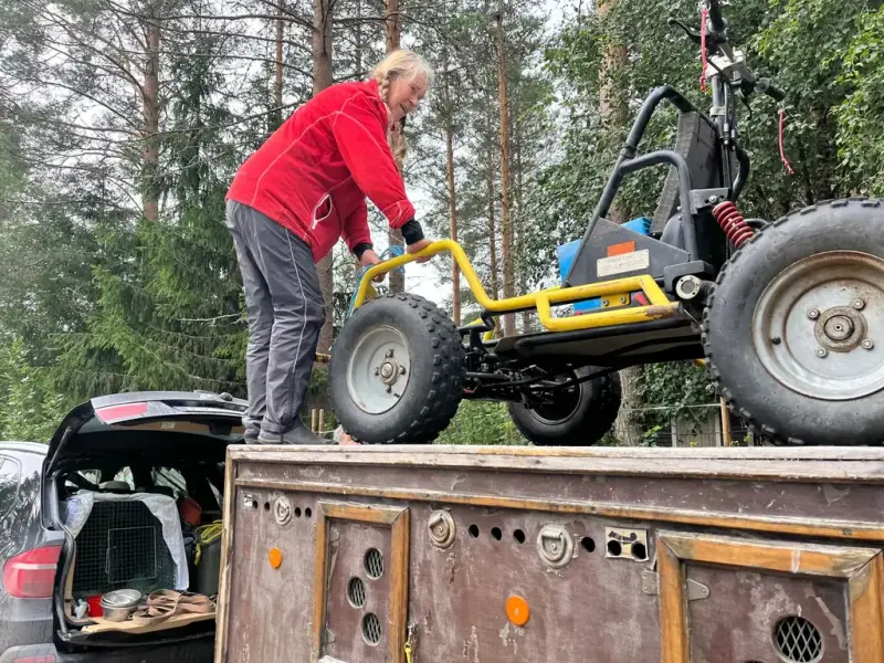 Kvinne på taket av en hundehenger, hun ruller på en vogn som skal trekkes av hunder 