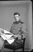 Porträtt av okänd ung man i militär uniform. Han sitter på en stol med en tidning i händerna.