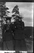 Porträtt av två okända kvinnor i hatt och mörk kappa stående på en höjd.