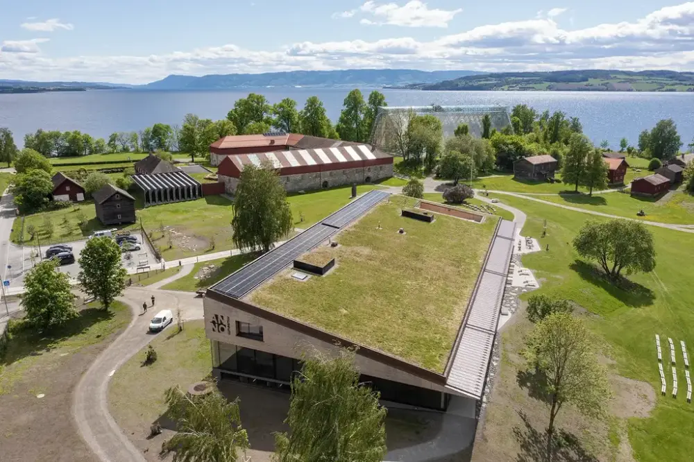 Dronefoto av Anno Domkirkeodden historiesenter med grønt torvtak, omgitt av grøntområder og trær om sommeren.