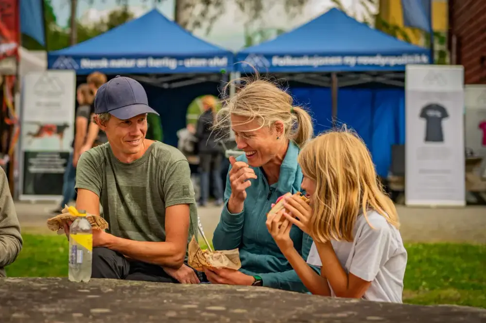 Familie sitter å spiser mat på en benk