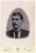 Porträtt av en man med mustach och slips.