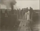 Folksamling på brygga vid en bolmande ångbåt.