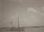 En mindre segelskuta med beslaget segel, två andra fartyg synliga på bilden.