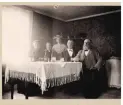 Gruppbild av ett sällskap på fem personer som sitter inomhus vid ett bord och ser ut att sitta och dricka.