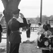 Drottning Elizabeth och hennes gemål prins Philip lämnar en limousin för att gå ombord på den kungliga yachten HMY BRITANNIA under sitt besök i Stockholm sommaren 1956. I förgrunden gör en svensk marinofficer honnör. En flottist från Stockholms örlogsstation skyldrar gevär.