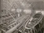Ett halvdussin båtar under byggnad i båthall.