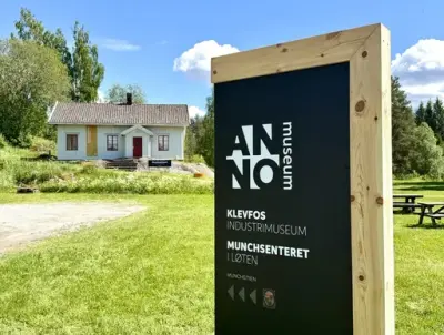 Stort skilt om Klevfos og Munchstien og hvitt hus i bakgrunnen
