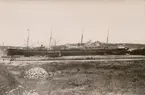 Fatryg vid kaj i Stockholms Frihamn/ Värtahamnen. Vy mot Lidingö, Villa Foresta. Stämpel 