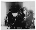 En man som spelar piano och tre personer som sitter intill och lyssnar.
