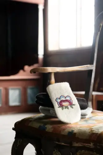 Sigdalsvotter, brodert med sigdalsroser hentet fra lokal rosemaling, liggende på en stol i salen i Eikjebygningen.