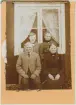 Familj sitter framför fönstret på ett bostadshus, Uppland 1905