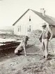 Man med kostym och en hund, står framför en arbetarbostad vid bygget av Älvkarleby kraftverk i Älvkarleby, omkring år 1906 (enligt text i album).