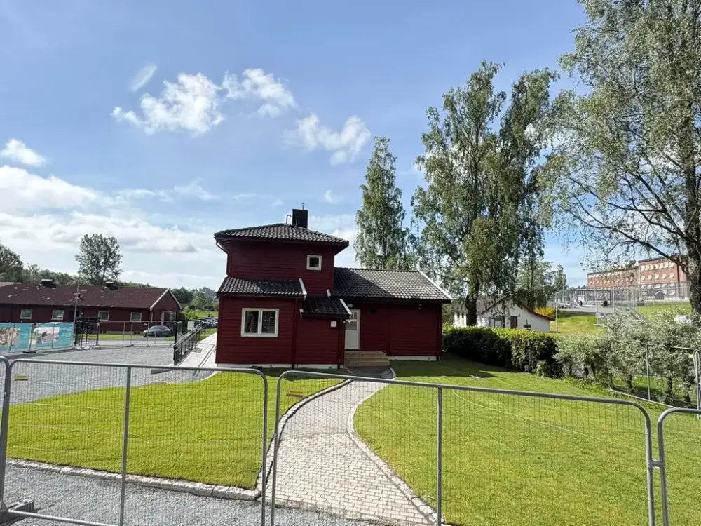 Bildet viser en grønn gressplen med byggegjerder rundt i bakgrunnen står det et rødt hud
