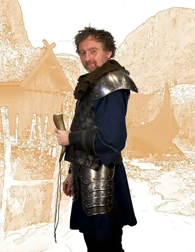 Mann med viking klær poserer foran en viking landsby.