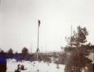 En linjemontör uppklättrad i en hög elstolpe av trä vid installation av el, vid byggandet av Älvkarleby kraftverk, omkring 1906 (enligt text i album).