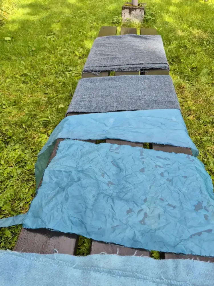 Flere stoffer ligger på en benk, de er nylig farget blått med vaid