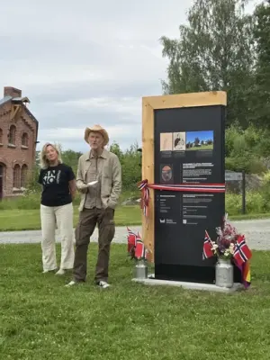 To mennesker står ved stort svart skilt og holder tale