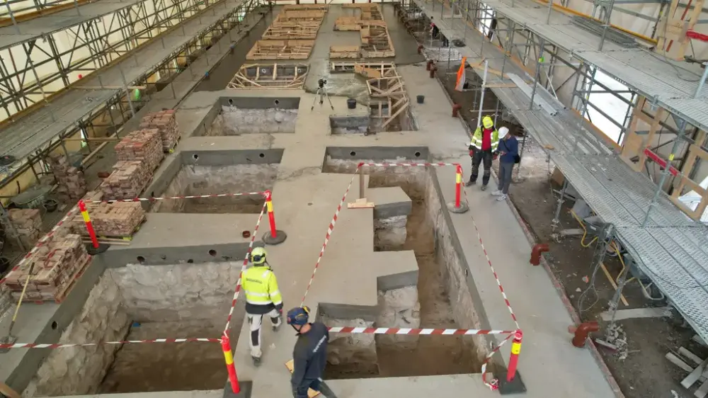 Grunnarbeid og muring i teglstein inne i et telt omgitt av stillaser