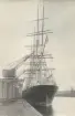 Segelfartyg vid kaj. Hamnkranar på kajen.