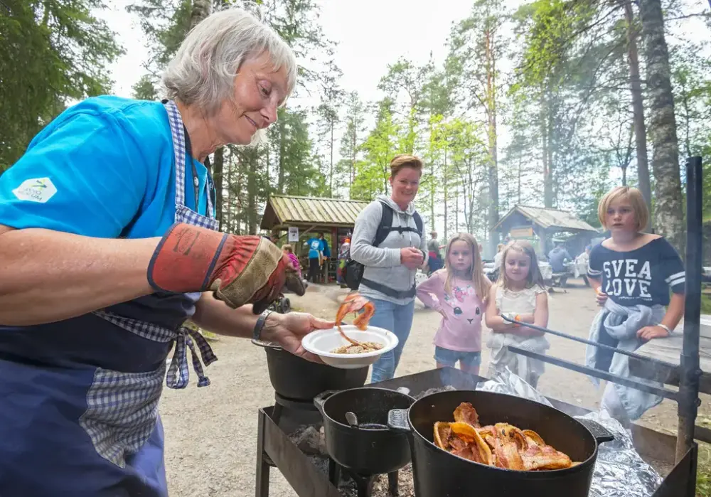 Mat lages i store gryter over åpen ild mens folk ser på under De nordiske jakt- og fiskedagene.