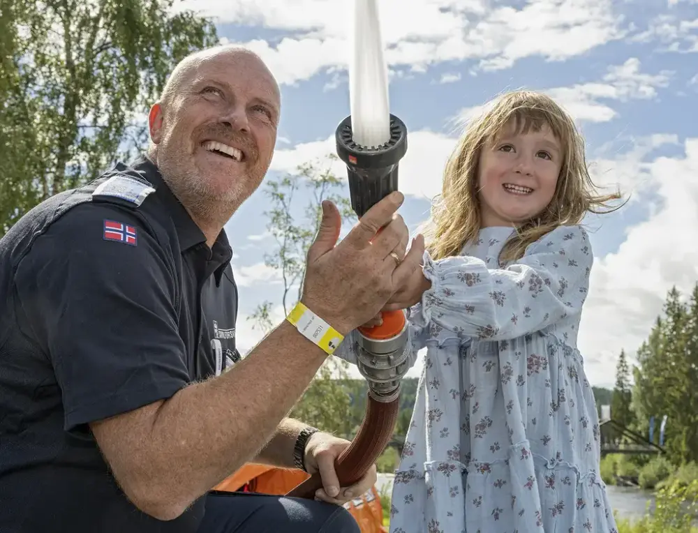 En smilende jente holder en brannslange sammen med en voksen under De nordiske jakt- og fiskedagene.