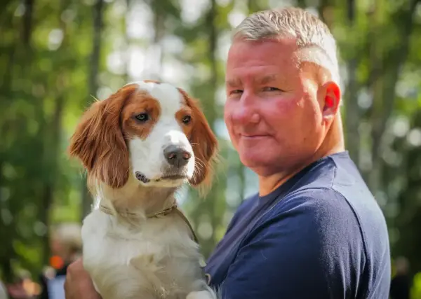 En smilende mann sammen med en spaniel utendørs under De nordiske jakt- og fiskedagene på Elverumsutstillingen.