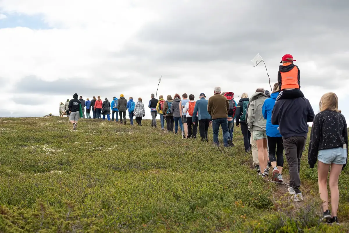En rekke med personer går oppover et fjell. 