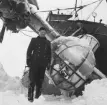 En miliitär står vid nosen  av flygplan B 18B nummer 18172, Röd David i Härnösands hamn med isbrytaren Ymer efter nödlandning på isen den 10 februari 1946. Tillhör Flygvapenmuseums bildarkiv.
