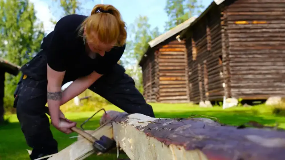 Kvinne som står med øks og hugger i en stokk