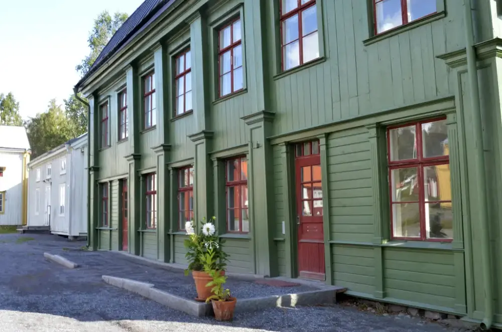 Ett grönt hus med röda fönster och dörrar.