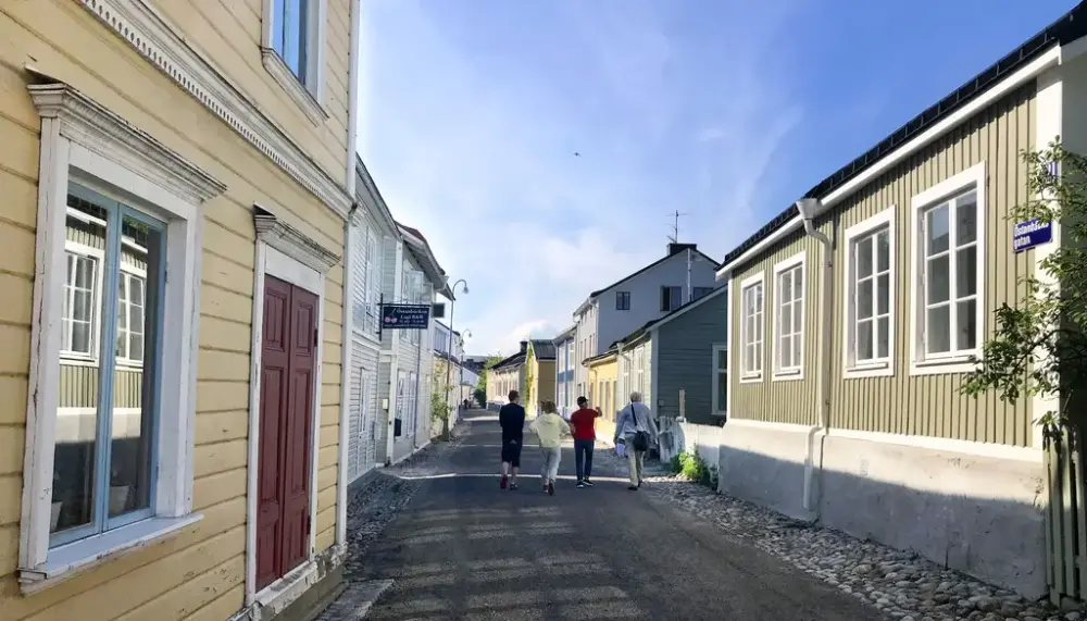 En gata med gammal trähusbebyggelse och några människor som promenerar.