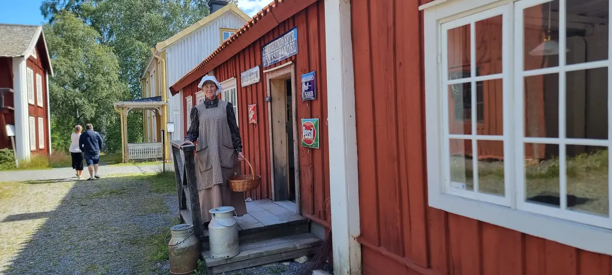 Kvinna i ålderdomliga kläder på trappan in till Handelsboden en sommardag